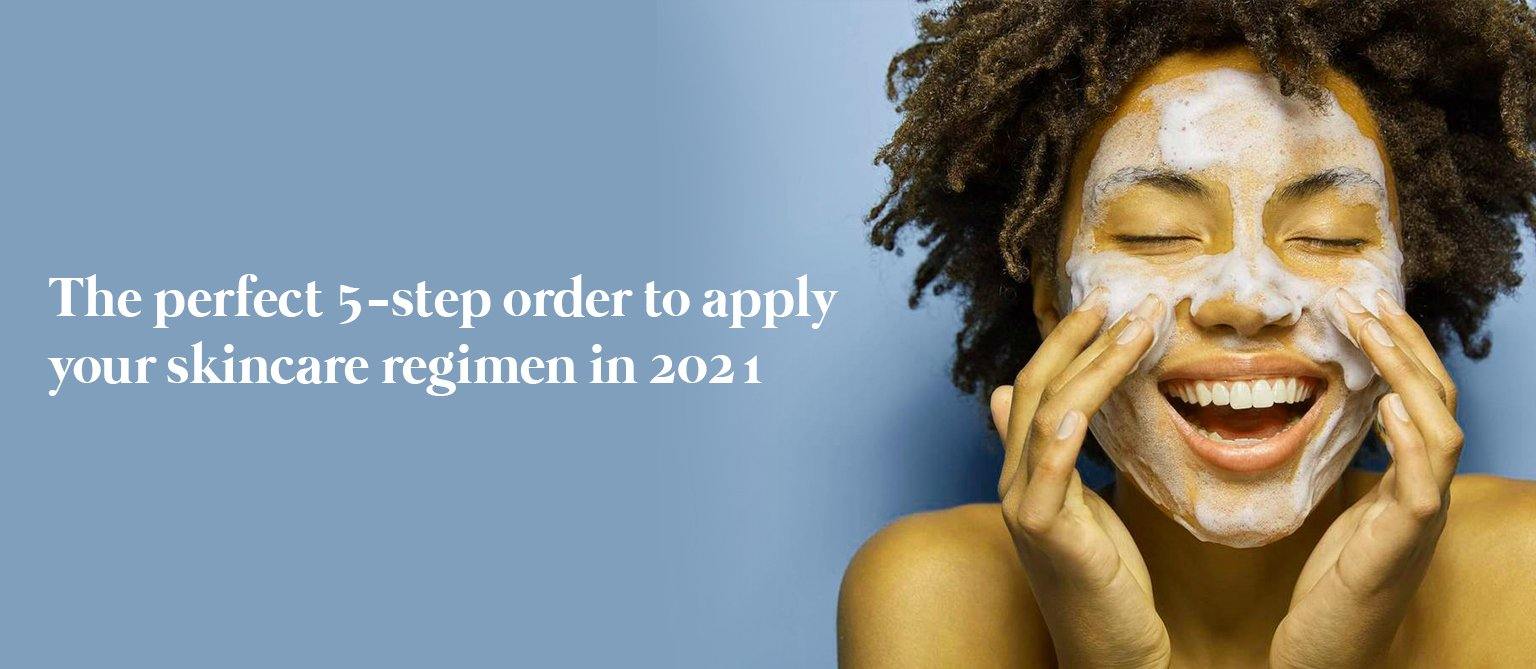 curly haired woman applying beauty cream to her face while smiling