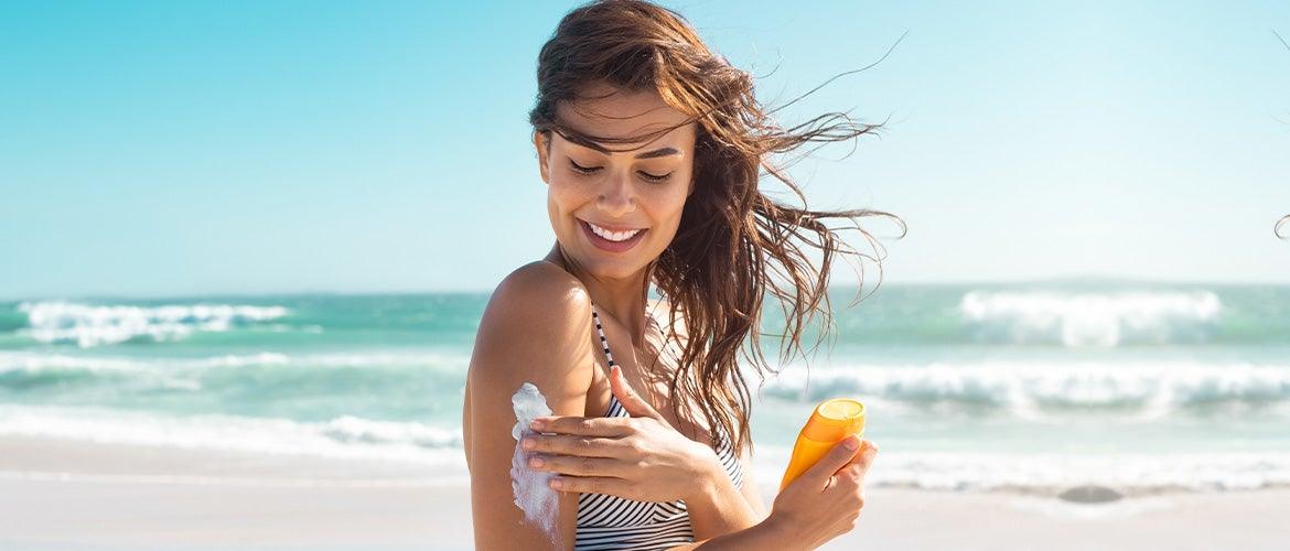 beautiful woman applying sunscreen at the beach during sun set